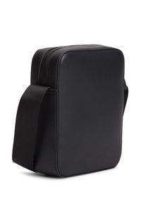 Μαύρη ορθογώνια τσαντάκι ώμου με στρογγυλεμένες άκρες, κλείσιμο με φερμουάρ και ρυθμιζόμενο φαρδύ λουρί από ύφασμα σε λευκό φόντο.