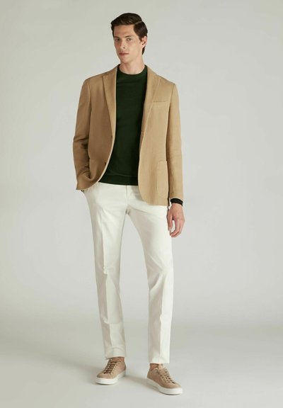 Beige Blazer mit Revers, grüner Pullover, weiße Hose und beigefarbene Sneakers. Glattes Material, taillierte Passform, minimalistisches Design.