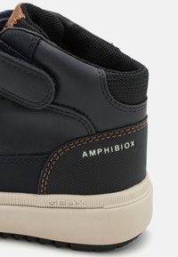 Sneaker montante noire avec une finition en cuir lisse, des accents en mesh, des coutures marron et une semelle en caoutchouc. Présente les marques "AMHIBIOX" et "GEOX".