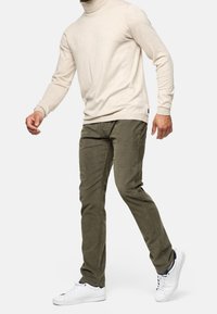 Beige turtleneck sweater parret med olivengrønne bukser og hvide sneakers. Sweateren har en ribbet hals; bukserne har lommer.