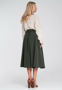 Zielona spódnica z korduroy o dopasowanej talii i zwiewnym kroju, zestawiona z lekkim swetrem i brązowymi butami na obcasie.
