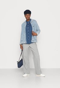 Jaqueta de ganga, camisa riscada azul, calças largas cinzentas, tênis brancos e um boné navy. Bolsa navy com alça de corrente.