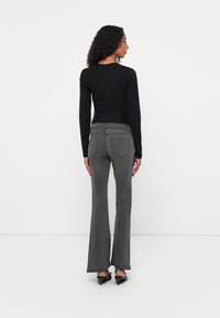 Jeans grigi flared con vita alta e design a cinque tasche, abbinati a un top attillato a maniche lunghe nero. Texture liscia, colori solidi.