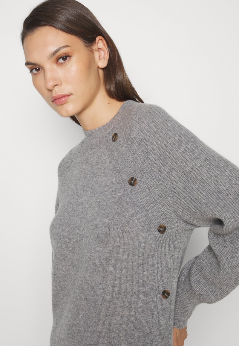 Szary dzianinowy sweter z okrągłym dekoltem, ściągaczowymi mankietami i pięcioma dekoracyjnymi brązowymi guzikami na lewym ramieniu. Miękka tekstura, luźny krój.