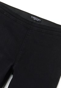 Pantalones jegging negros con etiqueta de cintura visible que dice "Republic of Denim" sobre un fondo blanco, mostrando la sección superior frontal.