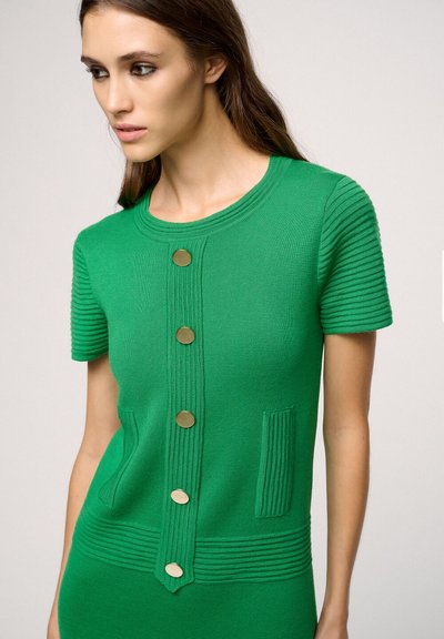 Top corto a maniche corte di colore verde in maglia, con scollatura rotonda, cinque bottoni dorati sulla parte frontale e accenti a righe testurizzate su maniche e orlo.