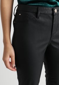 Černé kalhoty z umělé kůže s přiléhavým střihem, předními kapsami a zapínáním na knoflík, s jemným leskem a hladkou strukturou.