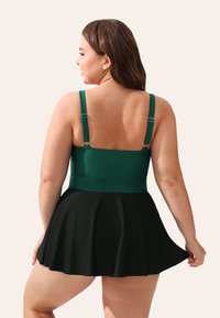 Groene tankini-top met verstelbare bandjes, gecombineerd met een zwarte uitlopende rok. Glad stof met een effen kleur ontwerp.