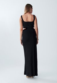 Black evening gown with a fitted silhouette, wide straps, and cut-out sides. Features a smooth texture and a full-length design.