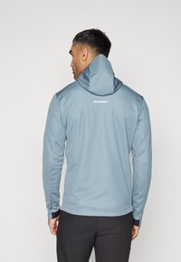 Lyseblå hoodie med blød tekstur, lange ærmer, justerbar hætte og sidelommer. Har et synligt logo på ryggen.