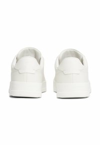 Zapatillas blancas de cuero liso con un diseño bajo. Presentan un collar acolchado y un logotipo de la marca embossado en el talón.