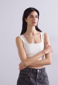 Top corto ajustado blanco con escote cuadrado, combinado con unos vaqueros negros de cintura alta. Textura suave, diseño minimalista y sin patrones visibles.
