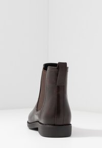 Botín Chelsea de cuero marrón con paneles laterales elásticos, puntera redondeada y un bajo tacón de goma negra. Textura suave con detalles de costura mínimos.