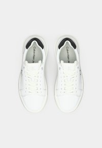 Un paio di sneakers bianche Calvin Klein con dettagli neri sul tallone, lacci bianchi e marchio visibile all'interno delle scarpe.