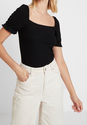 Black ribbed bodysuit with short puff sleeves and a square neckline, paired with light beige corduroy wide-leg pants.