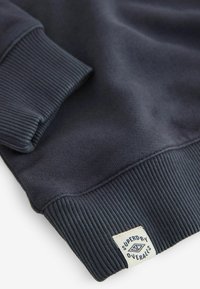 Felpa blu navy con polsini e orlo a coste, realizzata in tessuto morbido. Include un'etichetta con il dettaglio "Superdry Overalls".