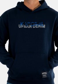 Felpa blu navy, in cotone, tasca a marsupio frontale, stampa del logo "Kaporal Urban Denim" in bianco e blu, polsini e orlo a costine.