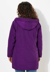 Giacca impermeabile viola con cappuccio, dotata di vita regolabile e superficie liscia. La vista posteriore mostra maniche lunghe e un design semplice.