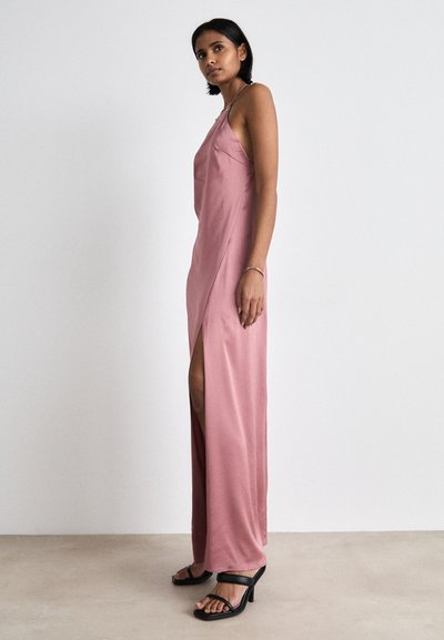 Rochie maxi din satin roz deschis cu o fante laterală și bretele subțiri. Modelul poartă sandale negre cu toc. Design simplu, elegant, fără embellishments.