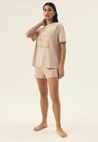 Beżowa bawełniana koszulka z krótkim rękawem i grafiką palmy, zestawiona z dopasowanymi wzorzystymi szortami. Miękka tekstura, luźny krój.
