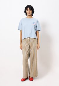 Hellblaues, kurzes T-Shirt mit kurzen Ärmeln, kombiniert mit weit geschnittenen, beigen gestreiften Hosen und roten Slippern.