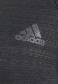 Czarna koszulka sportowa z teksturowanej tkaniny z delikatnym wzorem. Na przodzie znajduje się odbijająca srebrna logo Adidas.