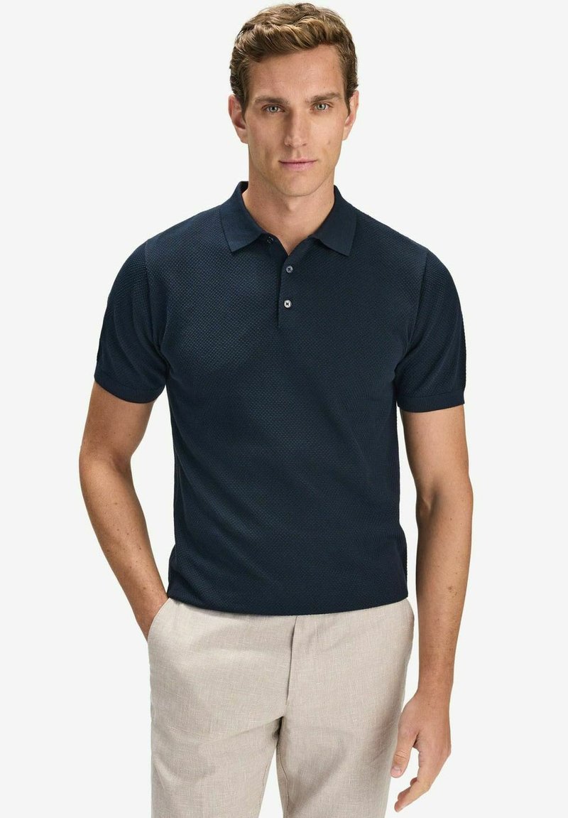 Marinblå polo-shirt med ett texturerat mönster, kort ärm och krage, med två knappstängning och en figurnära design. Ljust färgade byxor.