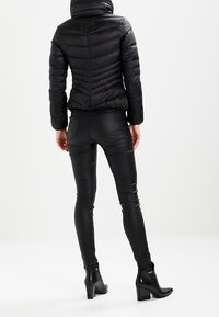 Mustapuffatakki, jossa on istuva muotoilu ja vaakasuuntainen tikkauskuvio, yhdistettynä mustiin tekonahkahousuihin ja nilkkabootseihin.