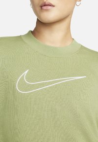 Pull court à manches courtes vert en tissu texturé, présentant un logo Nike blanc brodé à l'avant. Encolure ronde, coupe décontractée.