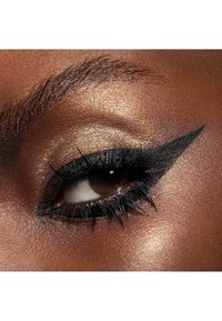 Close-up van een oog met gevleugelde zwarte eyeliner, glinsterende gouden oogschaduw, gedefinieerde wimpers en een gladde bruine huidtextuur.