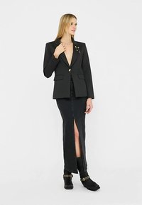 Sort blazer med dyb V-udskæring, enkelt knap og sidelommer, kombineret med en sort denimnederdel med frontslids og ankelstøvler.