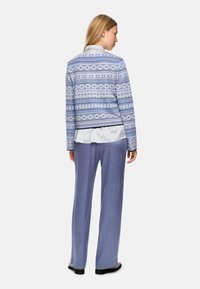 Blue patterned jacket with a curved hem, featuring circular designs and stripes, paired with soft blue wide-leg pants.