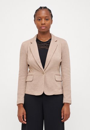 Beige bleiseri, jossa on jäsennelty muotoilu, yksittäinen napitus, kaksi etutaskua ja pitkät hihnat, käytetään mustan paidan päällä.