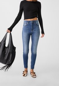 Höga blå skinny jeans, ribbad svart långärmad tröja, bruna och vita mönstrade ballerinas, svart läderhandväska med fransar.