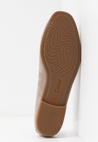 Chaussure en daim beige clair avec une semelle en caoutchouc, présentant un motif texturé et un logo embossé. Talon surélevé, fabriquée au Portugal.