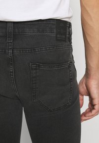 Černé džíny s těsným střihem, se značkovou koženou nášivkou na pase a prošíváním zadní kapsy. Hladká denimová textura.