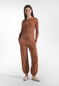 Maglia a costine color ruggine a maniche lunghe abbinata a pantaloni a vita elastica con coulisse e vestibilità ampia. Entrambi i capi hanno una texture liscia e polsini elastici alle caviglie.