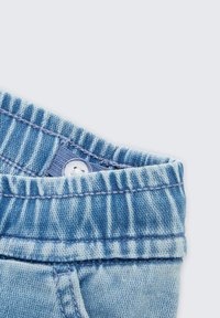 Jasnoniebieski pasek z denimu z widocznym przeszyciem i zapięciem na guzik. Charakteryzuje się miękką, lekko wyblakłą fakturą i żeberkowanym wzorem.