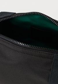 Εσωτερικό μαύρης υφασμάτινης τσάντας με λεία, πράσινη επένδυση; διαθέτει ανθεκτικό φερμουάρ κατά μήκος της κορυφής και ραμμένες λεπτομέρειες κατά μήκος των πλευρών.