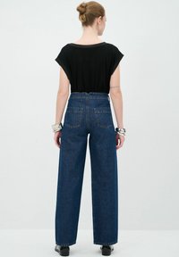 Černý top s krátkým rukávem v kombinaci s modrými džíny s vysokým pasem a širokými nohavicemi. Džíny mají dvě zadní kapsy a čistý lem.