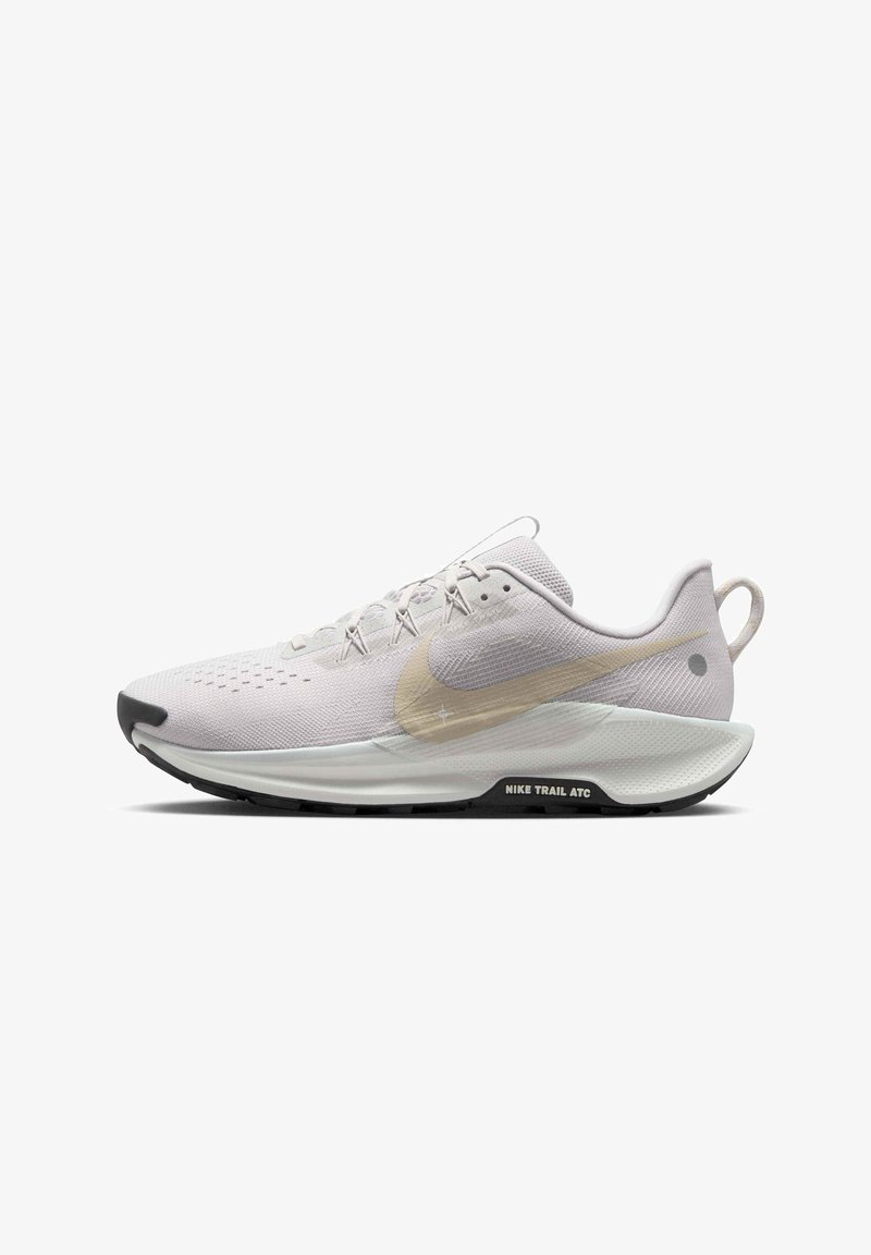 Hvid atletiksko i mesh-materiale med en metallisk gylden Nike swoosh, sort sål og struktureret detaljer på overdelen og hælen.
