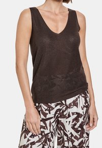 Brun ribbad tanktop med djup V-hals, tillverkad av ett mjukt, skimrande material, kombinerad med vita byxor med ett brunt lövmönster.