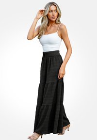 Zwarte tiered maxi rok van textuurstof, met een elastische tailleband en trekkoord. Gecombineerd met een witte aansluitende tanktop en sleehakken.