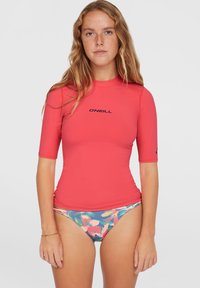 Červený krátky rukávový rash guard s logom, kombinovaný s modrými kvetinovými bikiny. Hladká textúra s priliehavým strihom pre vodné športy.
