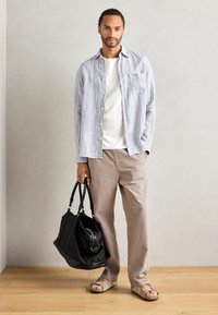 Casual outfit featuring a striped light blue and white button-up shirt, white t-shirt, beige pants, and black handbag, with tan sandals.