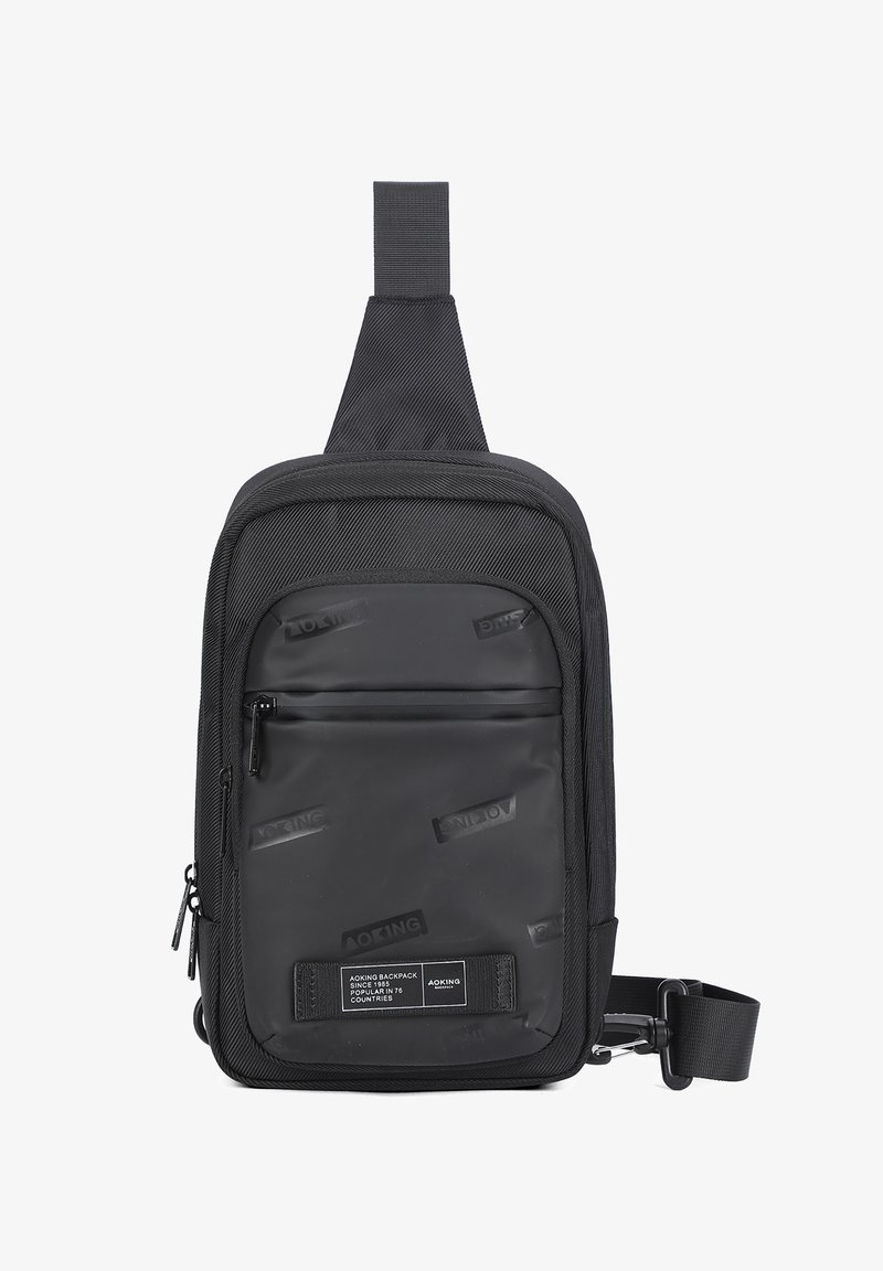 Borsa a tracolla nera realizzata in materiale resistente, con un pannello frontale liscio e loghi in rilievo, cinturino regolabile e scomparti con zip.