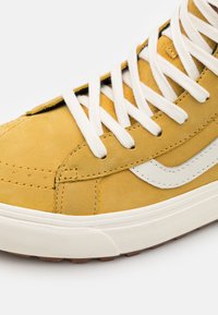 Sneaker in suède giallo con lacci bianchi, caratterizzato da una striscia bianca laterale, tomaia testurizzata e suola in gomma con un motivo a tratteggio puntinato.