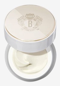 Hvit krem i en rund, hvit beholder med et blankt, gullbelagt lokk preget med et dekorativt "B" og våpenskjold design.