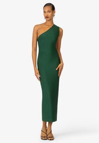 Robe verte ajustée à une épaule, fabriquée en tissu lisse, s'étendant jusqu'à mi-mollet avec une fermeture éclair sur le côté et des détails de coutures minimaux.