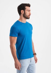 T-shirt blu brillante a maniche corte realizzato in un tessuto morbido, con scollatura rotonda e taglio dritto, abbinato a jeans chiari in denim.